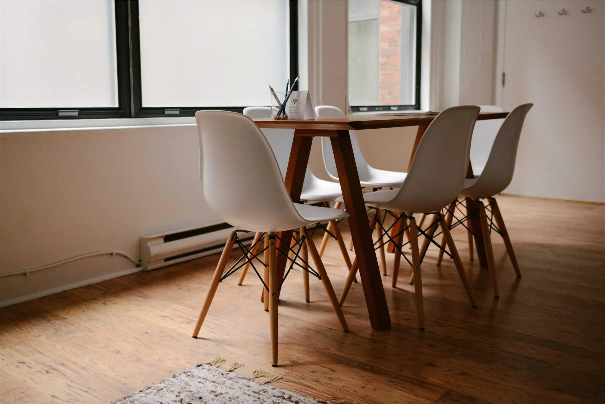 A bright room with plain painted walls, a wood floor and a table with white chairs.