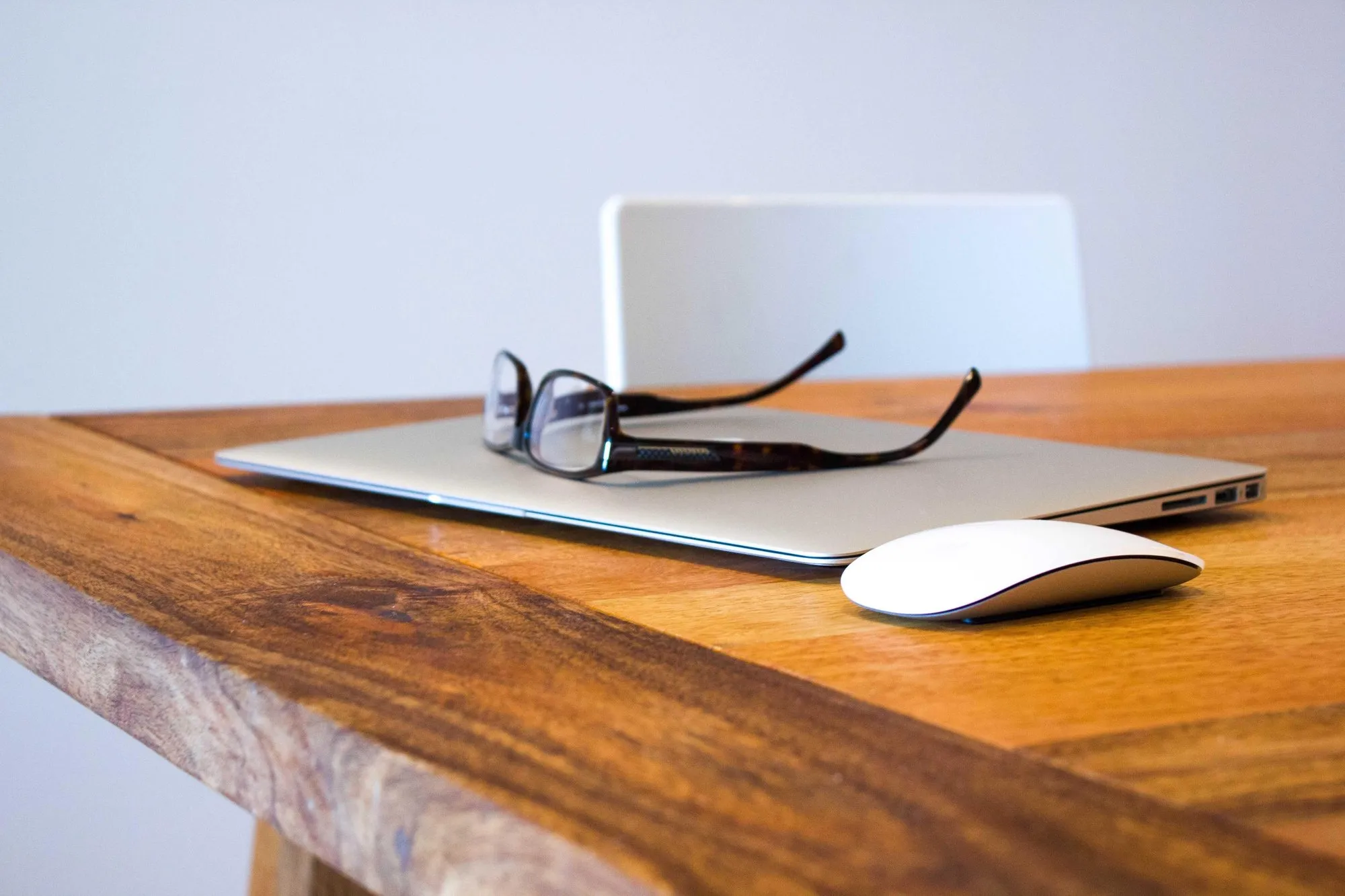 Reading glasses resting on a closed laptop on a wooden desk.