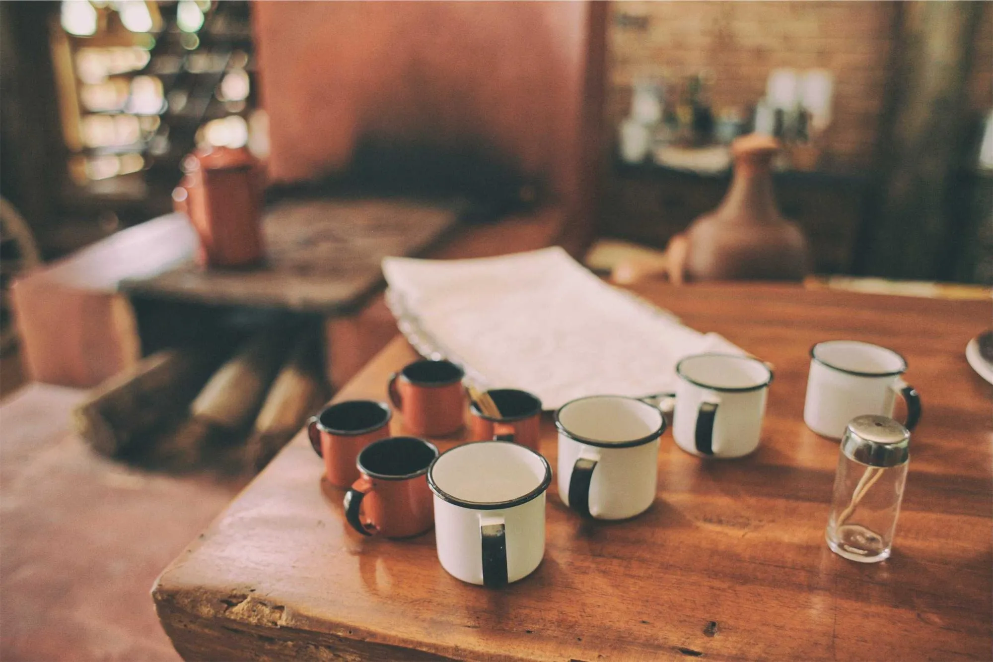 Enamel mugs and a folded cloth on a wooden table in a warm, rustic room