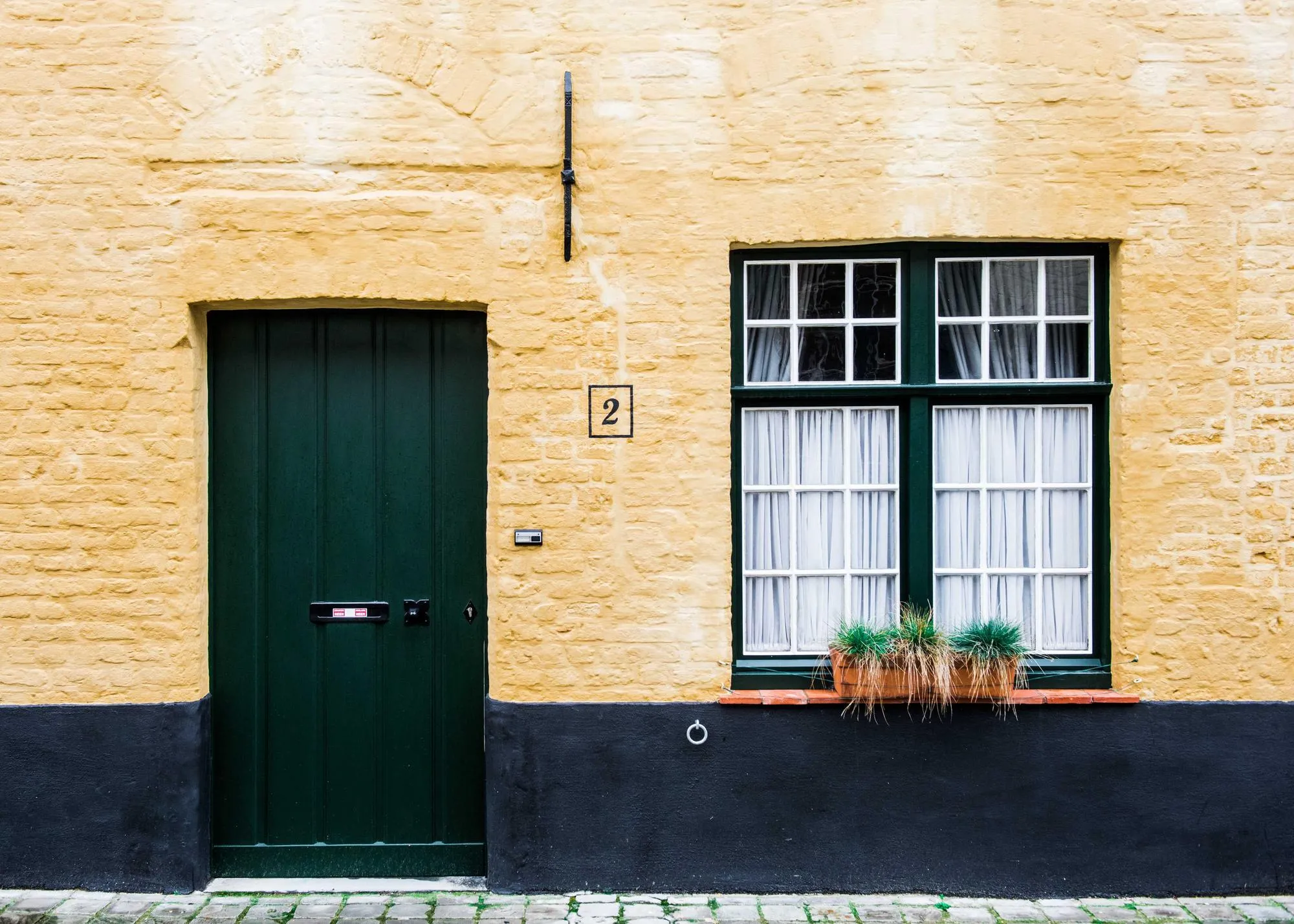 A green front door and a window with a flower box, set in a painted brick wall.